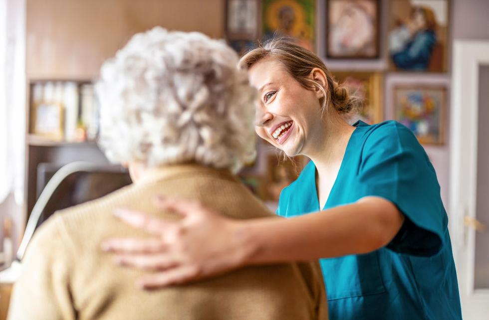 Pflegehelferin spricht mit älterer Frau und lächelt