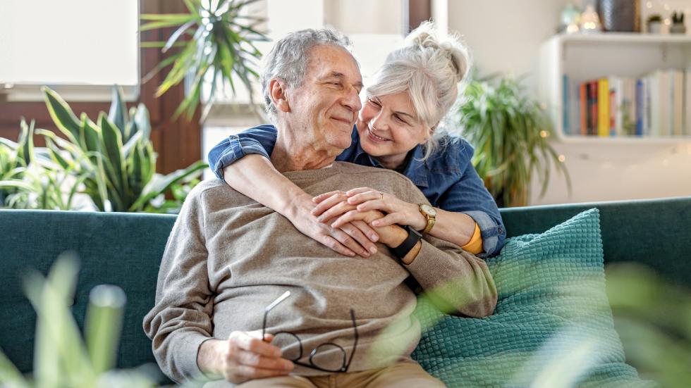 Frau umarmt Mann, der auf dem Sofa sitzt